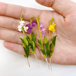 May include: Four artificial flower stems with white, purple, and yellow flowers. The stems are green and have small leaves.