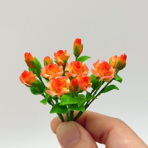 Puede incluir: Un ramo de pequeñas rosas artificiales de color naranja y amarillo con hojas verdes.