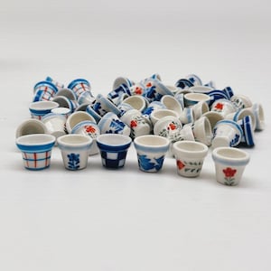 Może przedstawiać: Kolekcja małych, ceramicznych doniczek w różnych wzorach. Doniczki zdobione są niebiesko-białymi wzorami, w tym motywami kwiatowymi i geometrycznymi. Niektóre doniczki mają czerwone akcenty kwiatowe.