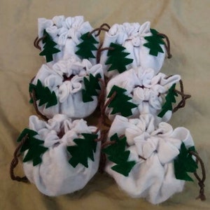 May include: Six white fabric drawstring bags with green felt pine tree designs. The bags are tied with brown string.