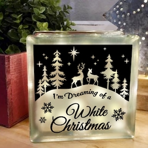 May include: A white glass block with a black background and a white design. The design features a snowy landscape with trees, deer, and snowflakes. The text "I'm Dreaming of a White Christmas" is written in a decorative font.