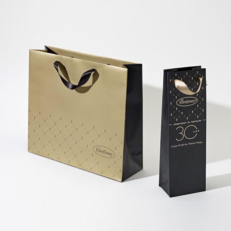 May include: Two gift bags, one gold with a black ribbon and the other black with a gold ribbon. Both bags have the logo "Eurofirany" and the text "Dziekujemy za wspolne 30 lat. Twoje wspomnienie, Nasza pasja."