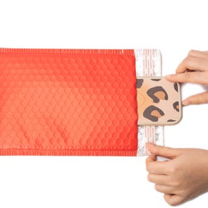 May include: A red padded envelope with a white and brown leopard print phone case inside. The case is being removed from the envelope.