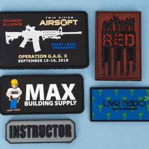 May include: A collection of rectangular patches with various designs and text. One patch features a white rifle graphic and text for "Midwest Alliance" and "Twin Cities Airsoft." Other patches include "MAX BUILDING SUPPLY," "RED," and "Instructor."