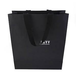 以下が含まれることがあります： 長方形の黒いショッピングバッグ。黒い布製の持ち手が付いています。バッグには白い文字で「LGVV」と書かれており、その下にテキストがあります。バッグはマットな素材で作られています。