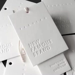 May include: White hang tags with embossed text. The top tag reads "Fashion" and the bottom tag reads "New Famous Brand". The tag in the middle reads "Thank you for buying our product".