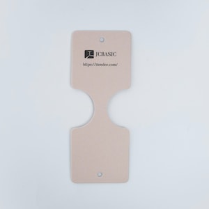May include: A light beige product tag with a unique shape, featuring a logo and the text "JCBASIC" and "https://itendee.com/". The tag has a hole at the top and bottom for attachment. The tag is made of a sturdy material.