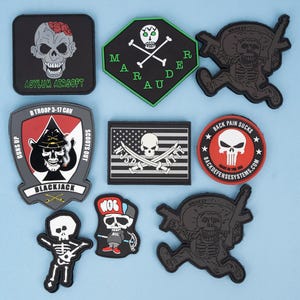 May include: A collection of black, gray, and red patches with skull designs. Some patches feature text like "Asylum Airsoft," "Mardi Gras," and "Back Pain Sucks." Other patches have military-themed designs.