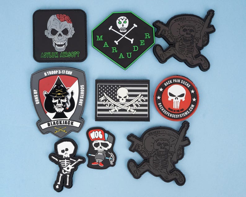 May include: A collection of black, gray, and red patches with skull designs. Some patches feature text like "Asylum Airsoft," "Mardi Gras," and "Back Pain Sucks." Other patches have military-themed designs.