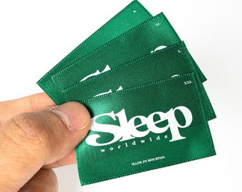 May include: Four green satin fabric labels with white text. The largest label reads "Sleep worldwide" and "Made in Houston". The other labels have size markings: "P", "XL", "L", and "XXL".