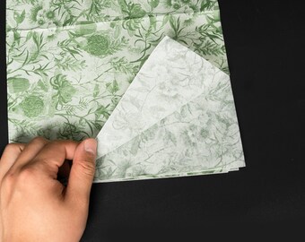 May include: A sheet of green and white patterned wrapping paper with a floral design. The paper is folded in half and the top layer is lifted to reveal the pattern underneath.
