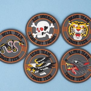 May include: Six round patches with various designs. The patches feature a snake, skull, tiger, eagle, and wolf. Each patch has a gray background with an orange border and the words "Tower Tech" and a team name. The patches are on a light blue surface.