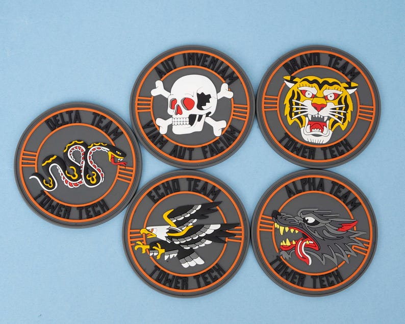 May include: Six round patches with various designs. The patches feature a snake, skull, tiger, eagle, and wolf. Each patch has a gray background with an orange border and the words "Tower Tech" and a team name. The patches are on a light blue surface.