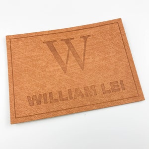 May include: A brown leather patch with the letter "W" and the name "WILLIAM LEI" embossed in a lighter brown colour.