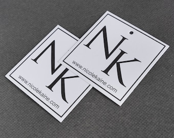 Pode incluir: Duas etiquetas quadradas brancas com bordas pretas e texto preto. O texto nas etiquetas diz "NK" e "www.nicolekaine.com".