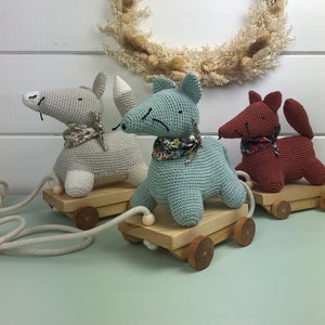 Può includere: Tre giocattoli di animali all'uncinetto su ruote di legno. Gli animali sono una volpe grigia, una volpe blu chiaro e una volpe marrone. Ogni animale ha una sciarpa con motivo floreale intorno al collo.