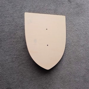 May include: A plain, light brown wooden shield with two small holes in the centre.