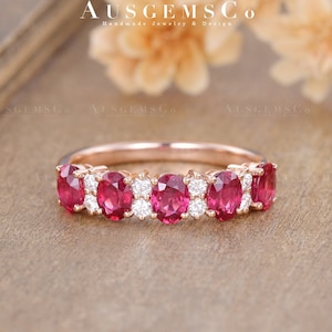 May include: A rose gold band ring with a row of oval-shaped ruby gemstones and smaller round diamonds set in the band.