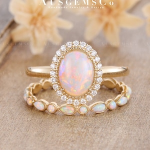 May include: A gold ring set with a large oval opal surrounded by a halo of smaller diamonds. The ring is paired with a matching band featuring a row of smaller opals.