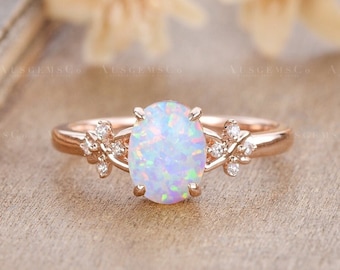 May include: A rose gold engagement ring featuring a white opal centre stone and small diamonds set on the band. The ring has a delicate floral design.