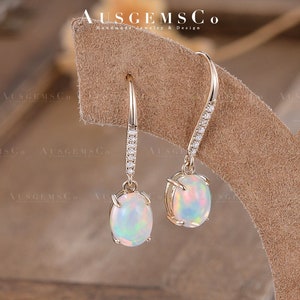Könnte beinhalten: Ein Paar goldene Opal-Ohrringe mit einer zarten Diamantenkette. Die Ohrringe haben einen perlmuttartigen Opal-Stein mit einem Regenbogen an Farben.