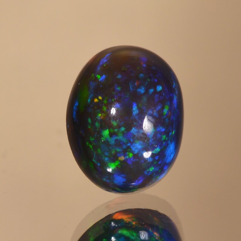 May include: A round black opal gemstone with green, blue and orange flashes of colour.