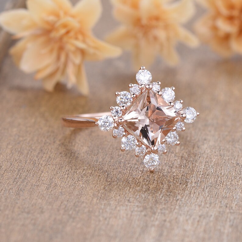 K&ouml;nnte beinhalten: Ein Verlobungsring aus Ros&eacute;gold mit einem quadratischen Morganit-Mittelst&uuml;ck, das von einem Heiligenschein aus kleineren runden Diamanten umgeben ist.