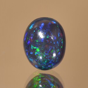 May include: A round black opal gemstone with green and blue flashes of colour.