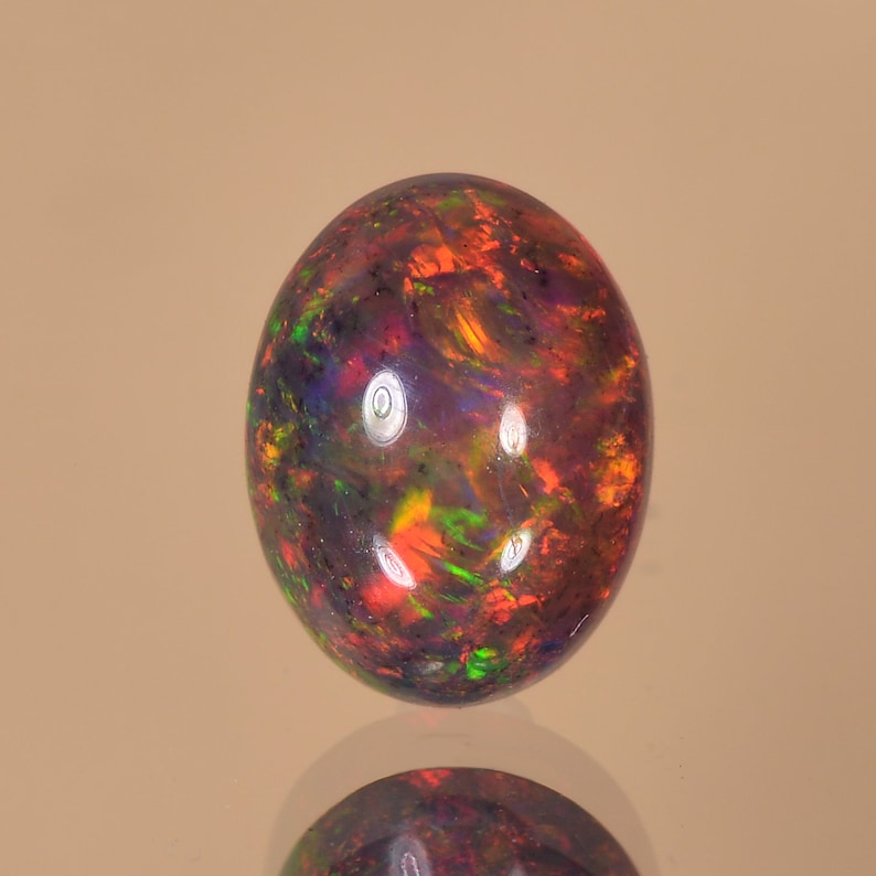 May include: A round, black opal gemstone with a vibrant display of red, green, and orange iridescent colours.