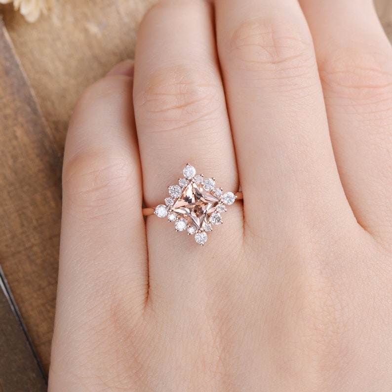 K&ouml;nnte beinhalten: Ein Verlobungsring aus Ros&eacute;gold mit einem quadratischen Morganit-Mittelst&uuml;ck, das von einem Halo aus kleineren runden Diamanten umgeben ist.