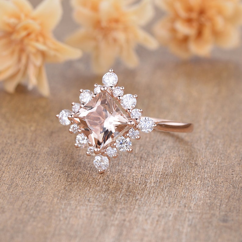 K&ouml;nnte beinhalten: Ein Verlobungsring aus Ros&eacute;gold mit einem quadratischen Morganit-Mittelst&uuml;ck, das von einem Heiligenschein aus kleineren Diamanten umgeben ist.