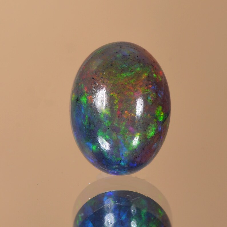 May include: An oval-shaped opal gemstone in dark grey with flashes of green, blue and red.