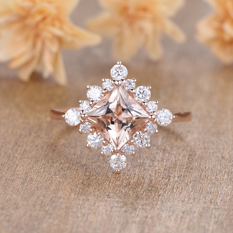 K&ouml;nnte beinhalten: Ein Verlobungsring aus Ros&eacute;gold mit einem quadratischen Morganit-Mittelst&uuml;ck, das von einem Heiligenschein aus kleineren runden Diamanten umgeben ist.
