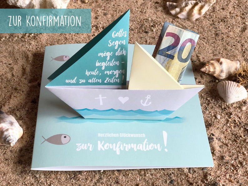May include: A light blue card with a white paper sailboat on top. The sailboat has a yellow sail and a twenty euro bill inside. The card has the text "ZUR KONFIRMATION" at the top and "Herzlichen Gl&uuml;ckwunsch zur Konfirmation!" at the bottom. The card is on a sandy surface.