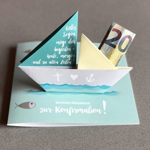 May include: A light blue card with a white paper sailboat on top. The sailboat has a yellow sail and a twenty euro bill inside. The card has the text "Gottes Segen m&ouml;ge dich begleiten - heute, morgen und zu allen Zeiten!" and "Herzlichen Gl&uuml;ckwunsch zur Konfirmation!" on it.