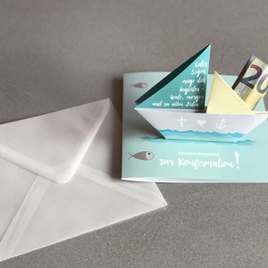 May include: A blue and white paper card with a pop-up paper boat. The boat has a cross, a heart, and an anchor on it. The card says "Colles Segen m&ouml;ge dich begleiten heute, morgen und zu allen Zeiten" and "zur Konfirmation!" There is a twenty euro bill in the boat.