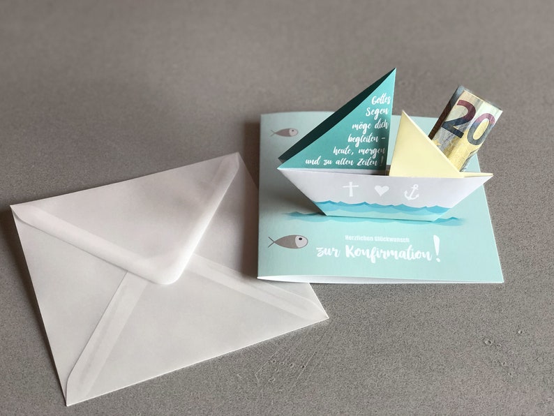 May include: A blue and white paper card with a pop-up paper boat. The boat has a cross, a heart, and an anchor on it. The card says "Colles Segen m&ouml;ge dich begleiten heute, morgen und zu allen Zeiten" and "zur Konfirmation!" There is a twenty euro bill in the boat.