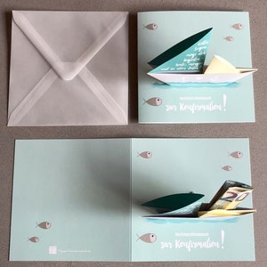 May include: A light blue pop-up card with a sailboat design. The sailboat is made of paper and has a green sail. The card has the text "zur Konfirmation!" on the front. The card is open and the sailboat is popped up. There are small fish on the front and inside of the card.