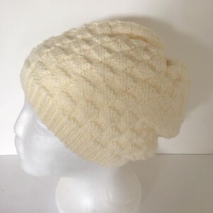May include: A cream-colored knitted beanie with a cable knit pattern.