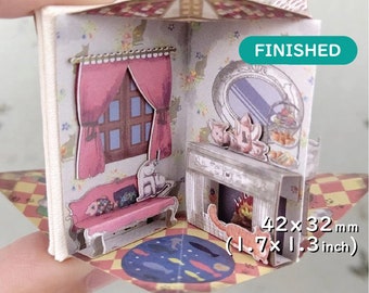 Puede incluir: Una casa en miniatura de papel con un sofá rosa, una chimenea y una figurita de gato. La casa mide 4,2 x 3,2 cm y está etiquetada como "TERMINADO".
