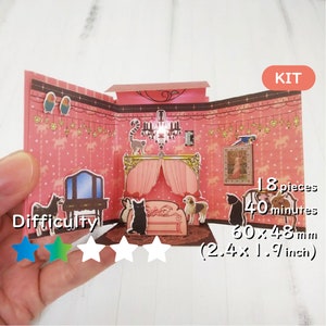 Puede incluir: Un kit de papercraft rosa y blanco con 18 piezas para ensamblar una habitación pop-up 3D. El kit incluye una lámpara de araña, una cama, un tocador y varias figuritas de animales. El kit está calificado con 4 de 5 estrellas por dificultad. El kit mide 60 x 48 mm (2,4 x 1,9 pulgadas).