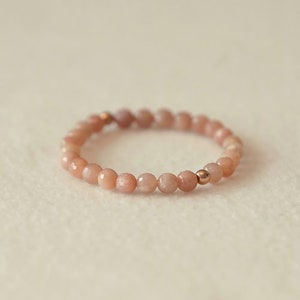 May include: A delicate bracelet made of light pink sunstone beads with a gold accent bead.