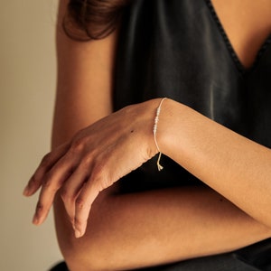 Peut inclure: Un bracelet d&eacute;licat avec de petites pierres gris clair sur une fine cordelette blanche. Le bracelet est nou&eacute; avec un simple n&oelig;ud.