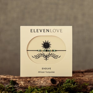 May include: A black string bracelet with African turquoise beads and a gold charm. The bracelet is packaged on a card with the brand name "ELEVENLOVE" and the words "EVOLVE African Turquoise".