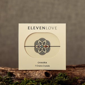 May include: A white card with the text "ELEVENLOVE" and "CHAKRA 7 Chakra Crystals" on it. A black string bracelet with seven colorful crystals is displayed on the card.