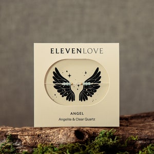 Peut inclure: Une carte blanche avec du texte noir qui dit "ELEVENLOVE" et une illustration en noir et blanc d'ailes d'ange avec des &eacute;toiles. Le texte sous l'illustration dit "ANGEL" et "Angelite & Clear Quartz".