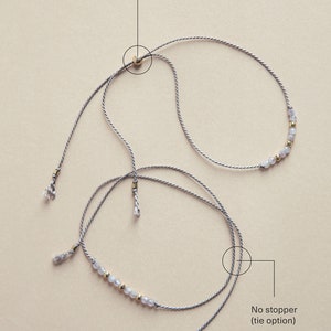 May include: Two gray cords with a row of small, light gray beads and gold beads. The cords are tied together at the top with a gold bead stopper. The cords are also tied together at the bottom, but without a stopper. "No stopper (tie option)" is written below the bottom tie.