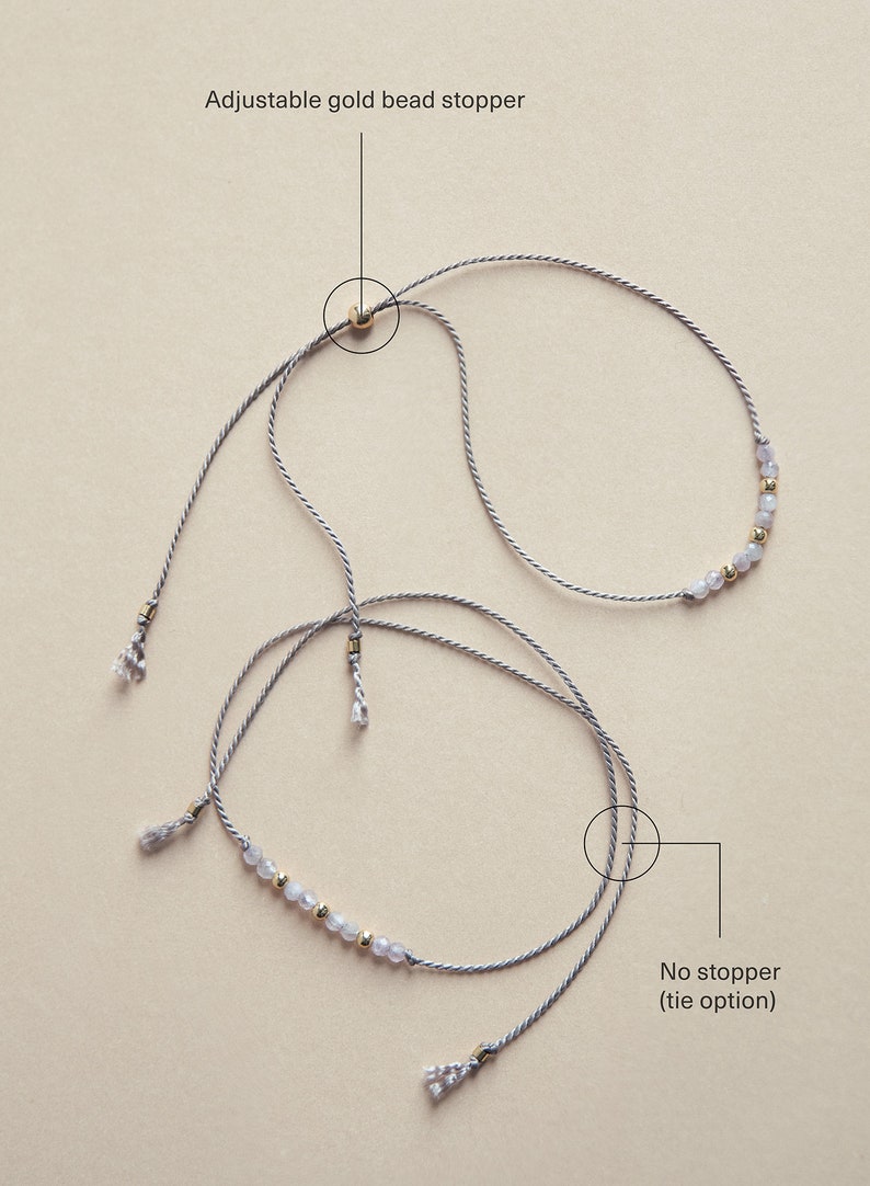 May include: Two gray cords with a row of small, light gray beads and gold beads. The cords are tied together at the top with a gold bead stopper. The cords are also tied together at the bottom, but without a stopper. "No stopper (tie option)" is written below the bottom tie.