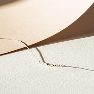 May include: A delicate necklace with a simple design featuring small clear beads and gold beads on a thin silver chain.