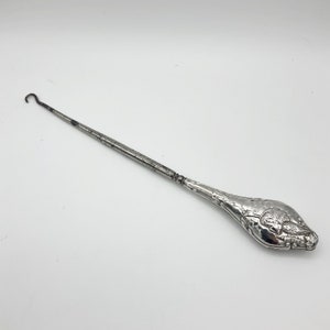 May include: A silver shoe horn with an ornate design. The handle is shaped like a bird with its wings spread.